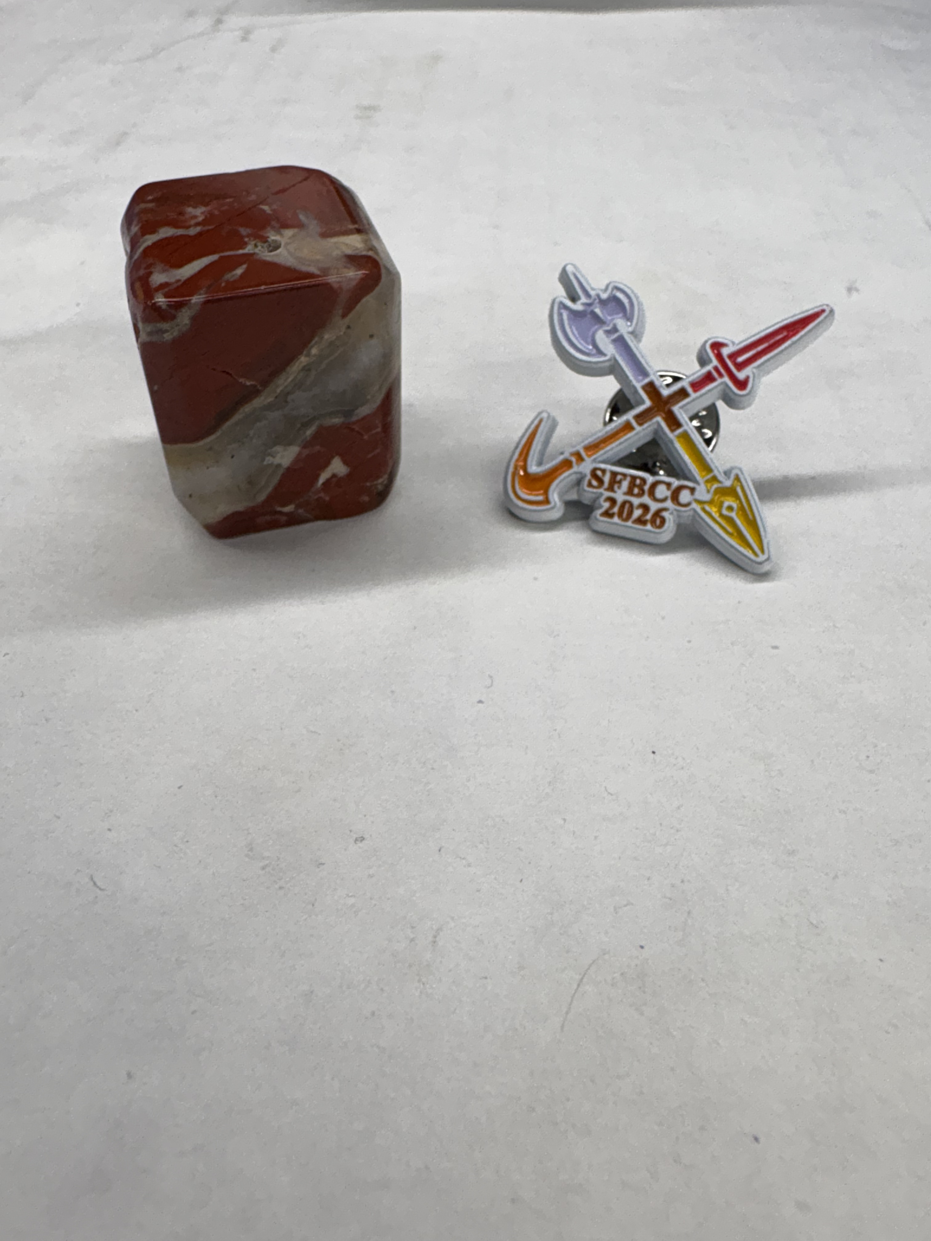 A red, black, and white marbled cube and a pin for SFBCC.